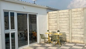 Eine Terrasse mit Schachbrettboden, einem Tisch mit Stühlen und einer Glastür zu einem Innenbereich mit Sitzgelegenheiten.