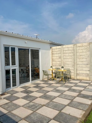 Eine Terrasse mit Schachbrettboden, einem Tisch mit Stühlen und einer Glastür zu einem Innenbereich mit Sitzgelegenheiten.