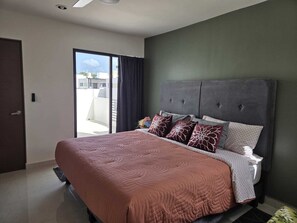 Ein Schlafzimmer mit einem Bett, einer dunkelgrünen Wand und Blick durch ein Fenster.