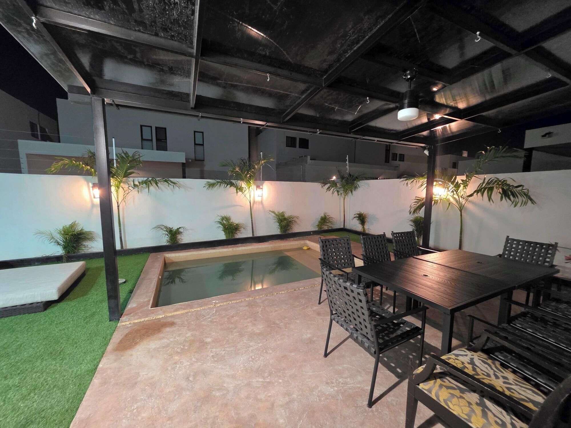 A poolside area with a table and chairs, surrounded by a low wall with plants.