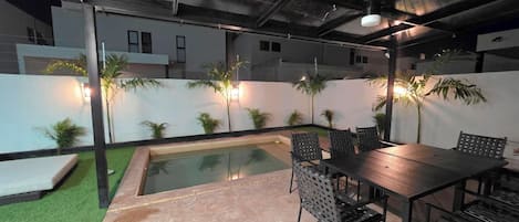A poolside area with a table and chairs, surrounded by a low wall with plants.