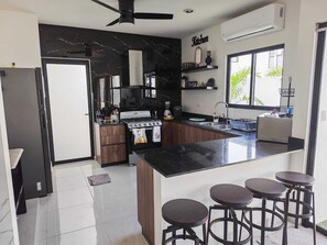 A modern kitchen with a central island, bar stools, a built-in oven, and a window providing natural light. - 3-bedroom house (Mérida)