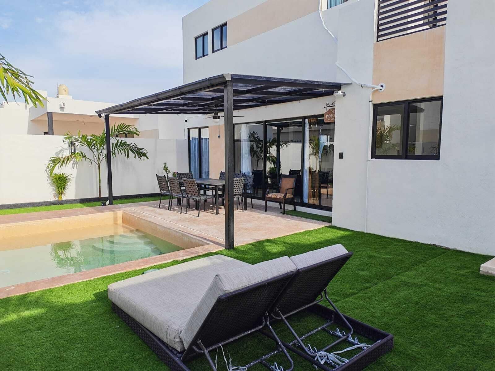 A modern outdoor patio with a pool, a covered seating area, and a lounge chair.