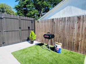 A backyard with a wooden fence, a grill on a stand, a potted plant, and bags of charcoal. - Cozy 1-bedroom apartment in beautiful Tampa with AC (Tampa)