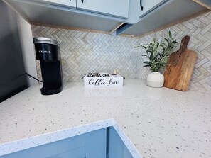 Une cuisine équipée d’une machine à café, d’un panneau indiquant un bar à café, d’une plante en pot et d’une planche à découper en bois.