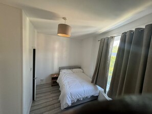 A bedroom with a bed, a ceiling fan, a window with curtains, and a door. - Spacious 4BR 4bath With Free Parking in Manchester (Manchester)