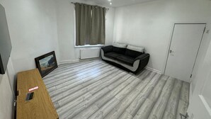 A room with a grey sofa, a wooden table, a television, and a window with curtains. - Spacious 4BR 4bath With Free Parking in Manchester (Manchester)