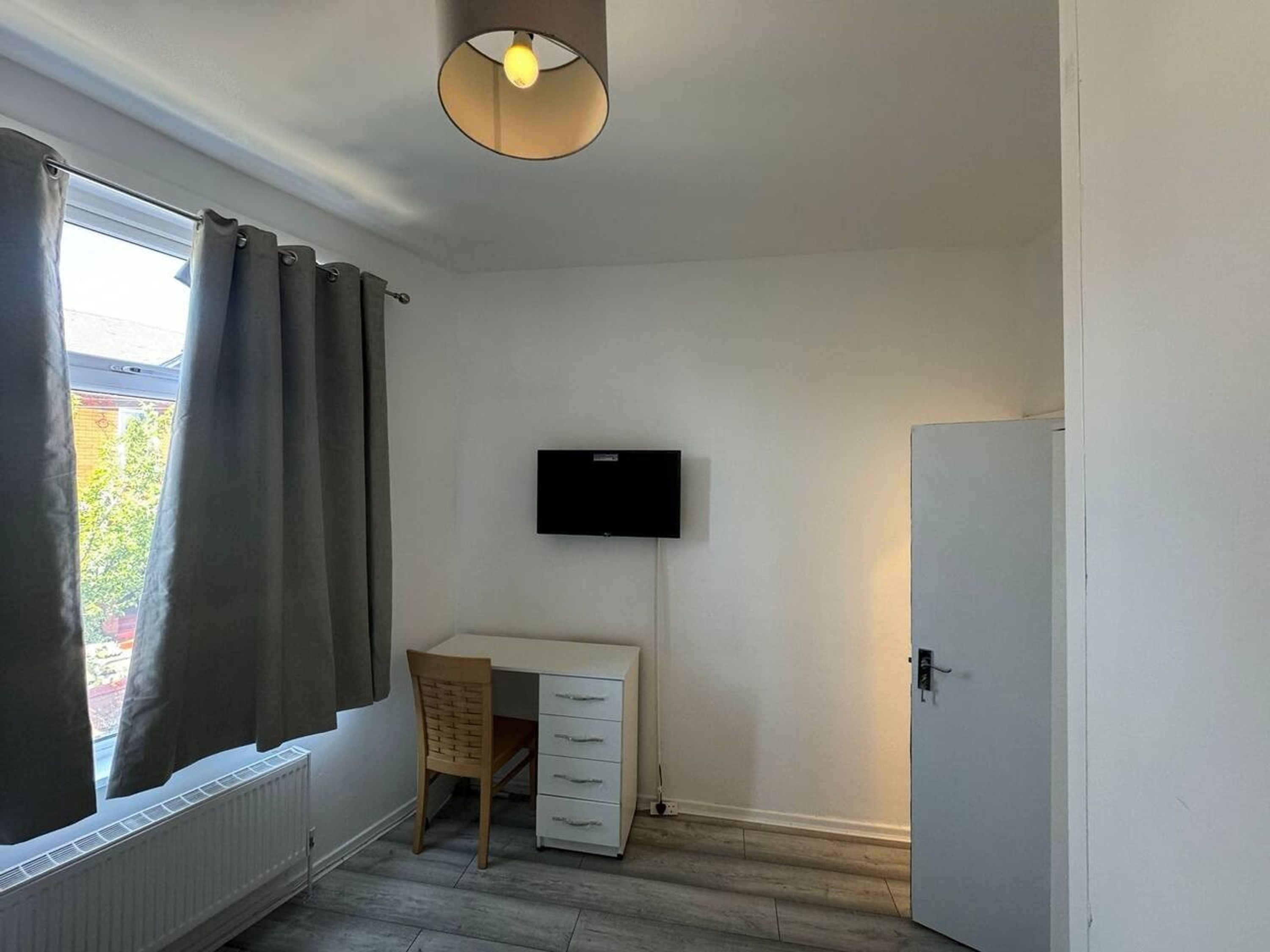 Une pièce comprenant un bureau, une chaise, un radiateur et un téléviseur fixé au mur.