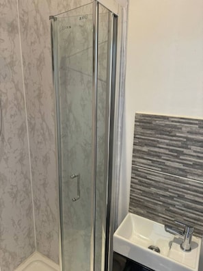 Ein Badezimmer mit Duschkabine aus Glas, einem weißen Waschbecken und einer gefliesten Wand.