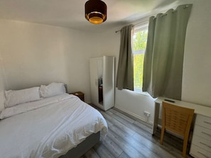 Ein Schlafzimmer mit Bett, Kleiderschrank, Schreibtisch und einem Fenster mit Vorhängen.
