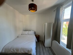 Ein Schlafzimmer mit einem Bett, einem Nachttisch, einem Kleiderschrank und einem Fenster mit Vorhängen.