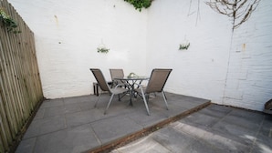 Eine Terrasse mit Tisch und Stühlen, einer weißen Wand und einem Holzzaun.