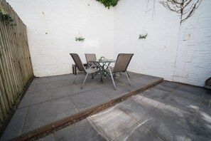 A patio with a table and chairs, a white wall, and a wooden fence. - Premium 3 Bed Cardiff City Sleeps 9 With Free Parking (Cardiff)