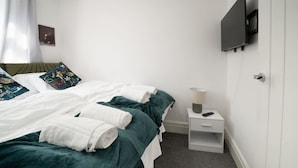 Ein Hotelzimmer mit Bett, Nachttisch mit Lampe und an der Wand montiertem Fernseher.