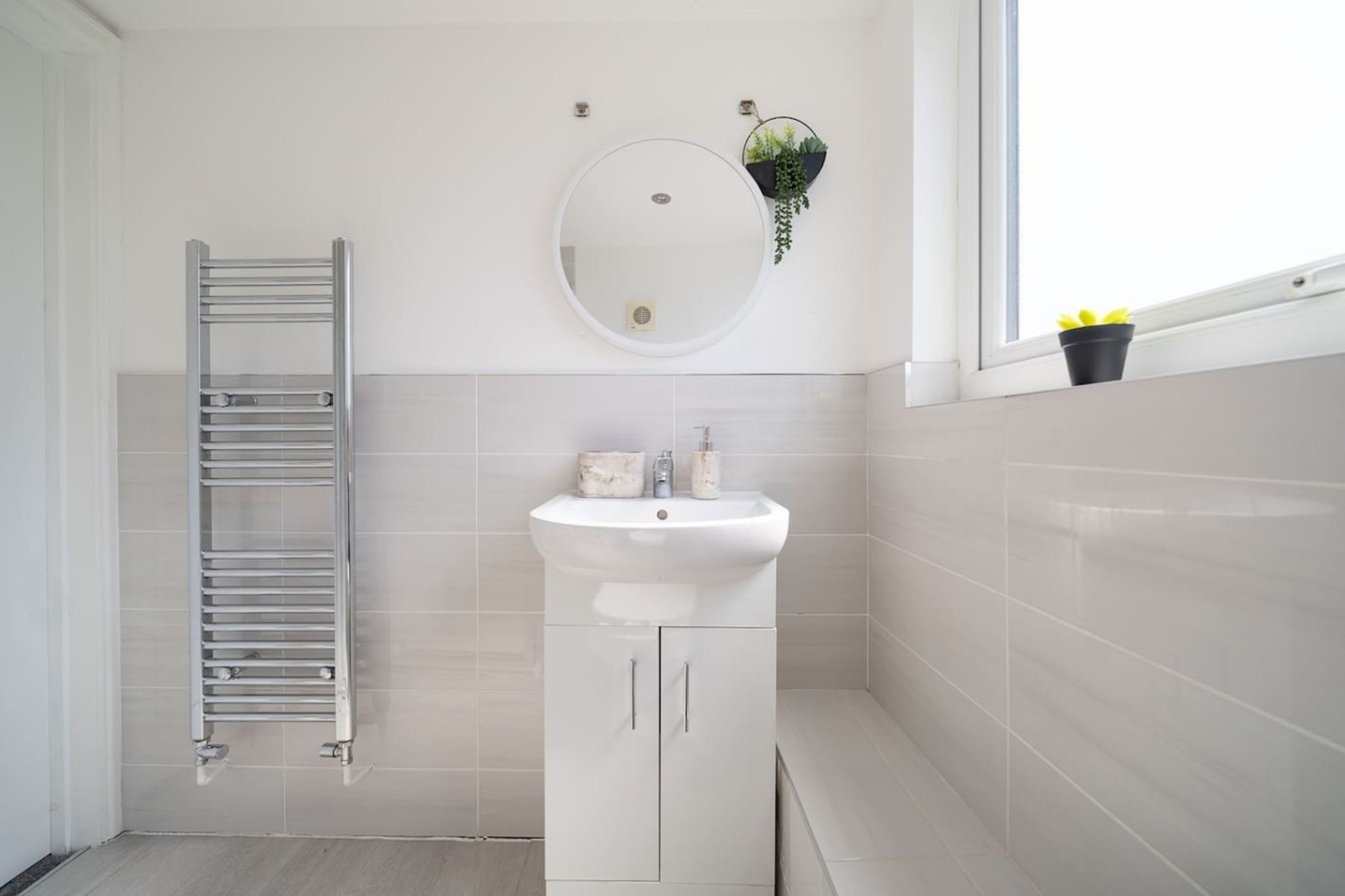 A bathroom with a white sink, a mirror, a towel rack, and a window with a plant on the sill.