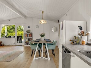 Eine moderne Küche mit Essbereich, weißen Schränken, einem Holztisch und Blick ins Grüne.