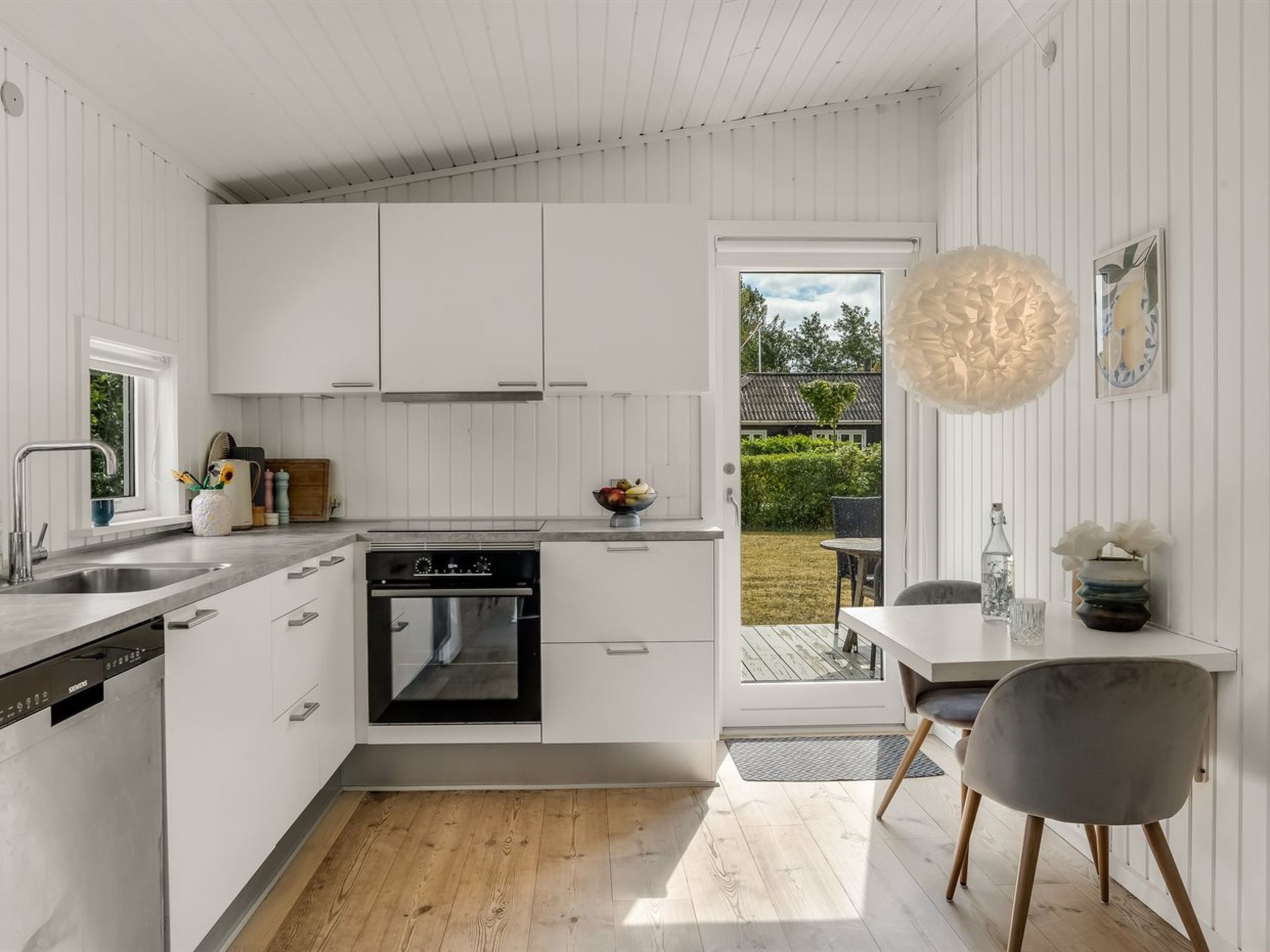 A modern kitchen with white cabinetry, a built-in oven, and a dining area with a table and chairs.