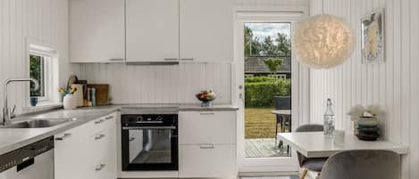 A modern kitchen with white cabinetry, a built-in oven, and a dining area with a table and chairs.