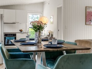 A dining area with a wooden table set for four, surrounded by teal chairs, and a vase with flowers on the table. - "Ulli" - 350m from the sea by Interhome (Grenaa)