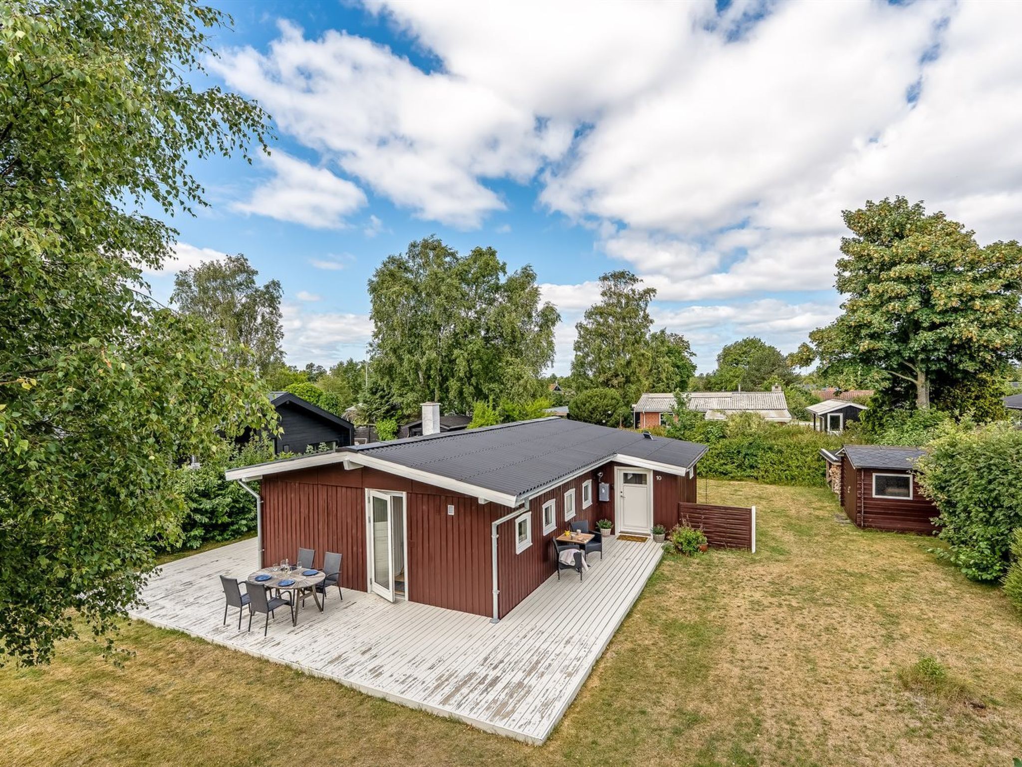A single-story wooden cabin with a deck, a small attached building, and a grassy yard.