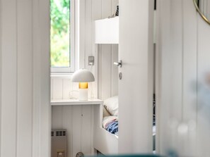 A bedroom with a bunk bed, a bedside table with a lamp, and a window with a view of greenery.