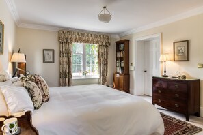 A well-appointed bedroom with a large bed, a dresser, a nightstand, a lamp, a bookshelf, and a window with curtains. - The Orangery -  Bridgnorth , Shropshire (Bridgnorth)