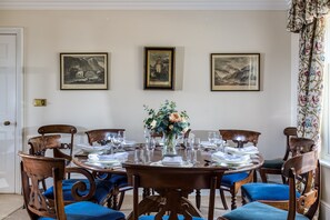 A dining room with a round table set for six, flanked by six wooden chairs with blue upholstery. Three framed historical paintings are hung on the wall above the table. - The Orangery -  Bridgnorth , Shropshire (Bridgnorth)