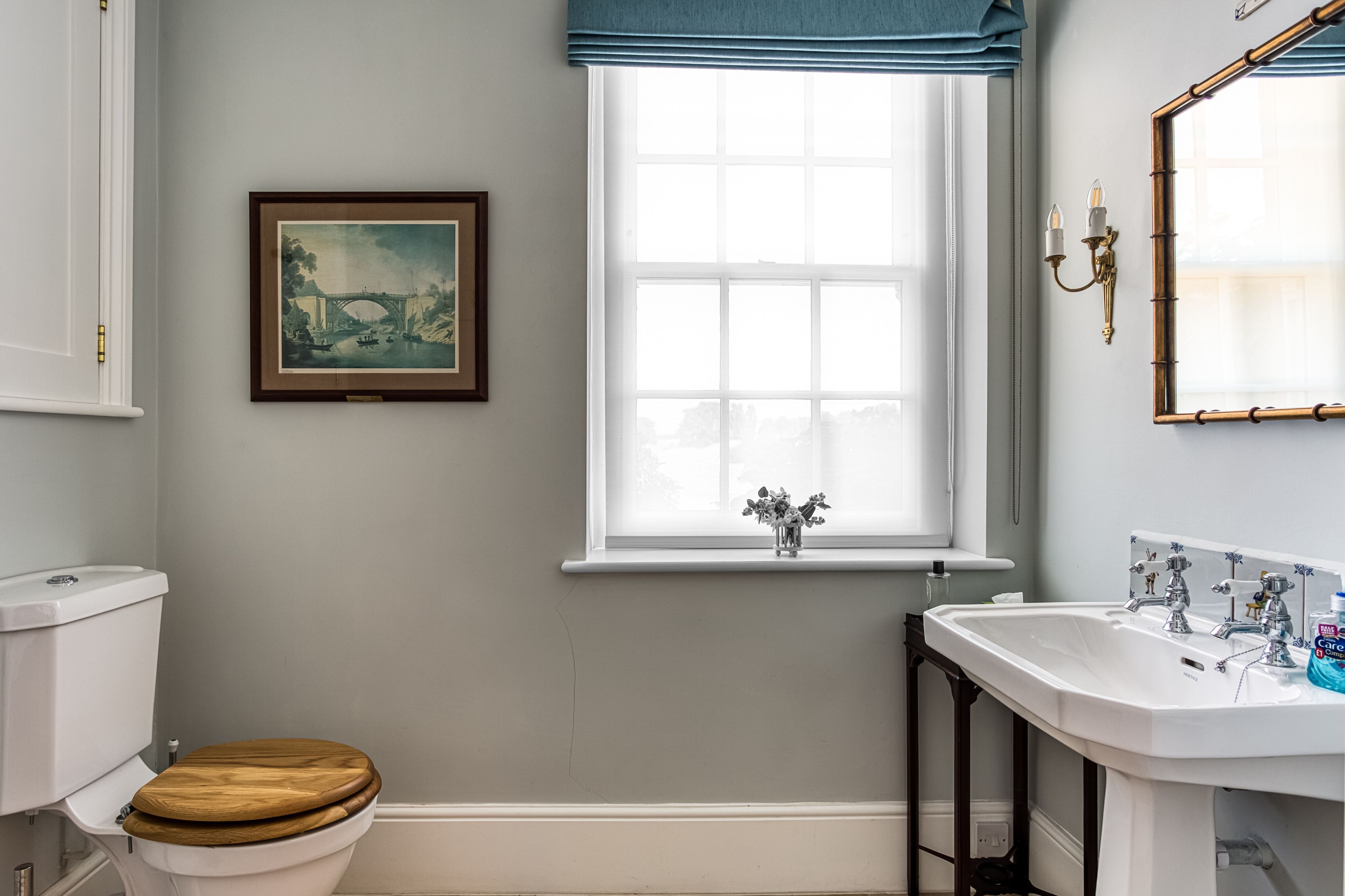 Un baño con inodoro, una ventana con vistas, un lavamanos y un cuadro enmarcado en la pared.