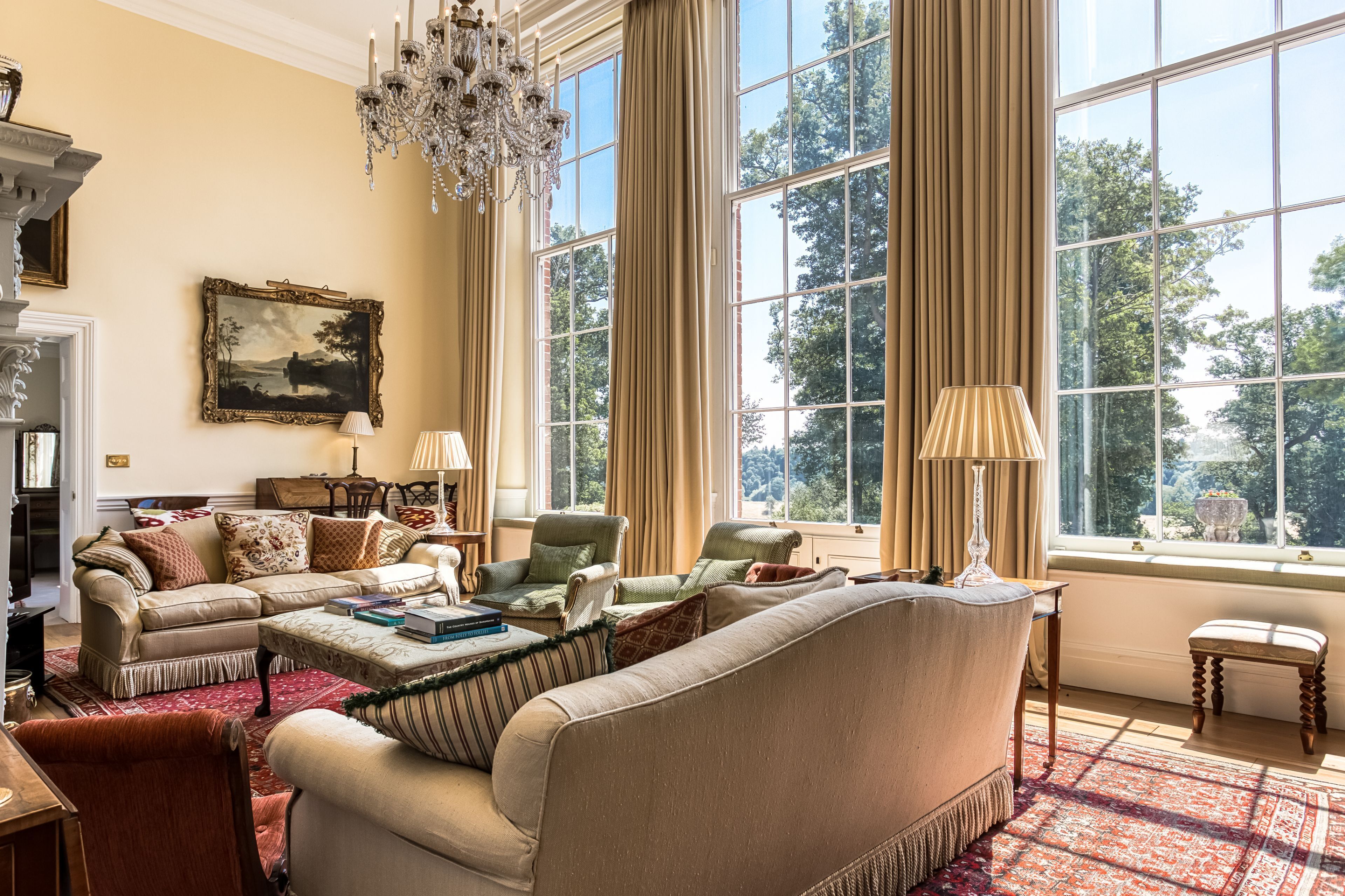 A spacious living room with a large window, a chandelier, and a painting on the wall.