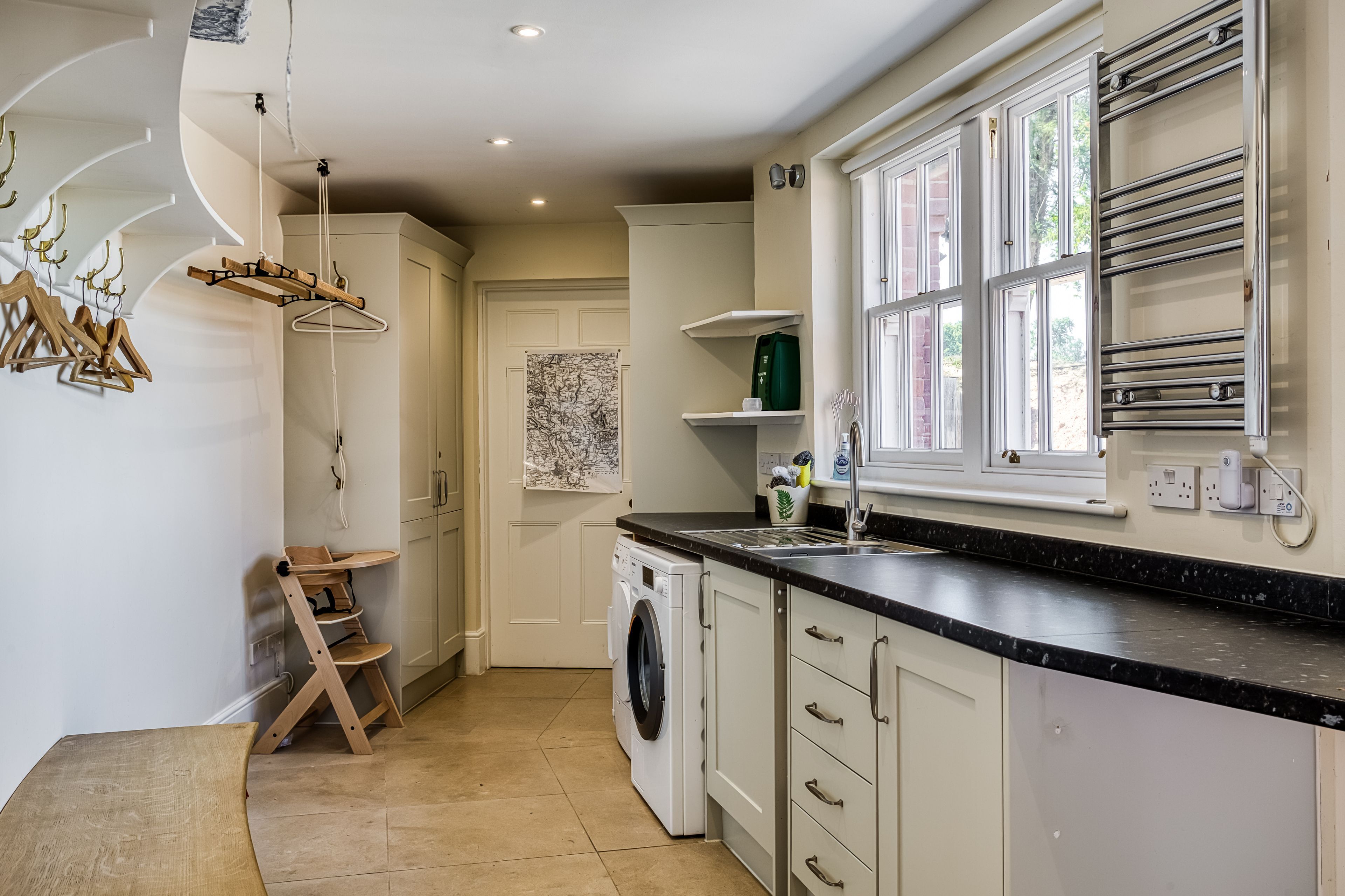A kitchen with a washing machine, a drying rack, and a window with a towel rack.