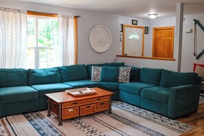 A living room with a green sectional sofa, a wooden coffee table, and a patterned rug. - 3 bedroom, 2 bath house with endless activities (Bridgton)