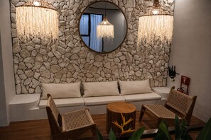 Ein Zimmer mit Stehwänden, einem runden Spiegel, einer Couch, zwei Korbstühlen, einem Holztisch und hängenden Lampen.