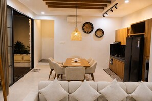 Uma sala de estar moderna com sofá, mesa de jantar e cadeiras. Há uma área de cozinha com geladeira e armários.