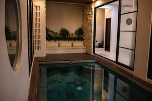 Piscina com muro de pedra e área de estar acolchoada.