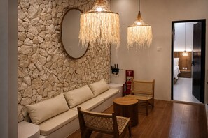 A modern interior with a stone wall, a sofa, two wicker chairs, a round table, and a hanging light fixture. - Cala Vista Villa Tumbak Bayuh Bali. Spacious 3BR Villa for Families & Groups. (Tumbak Bayuh)