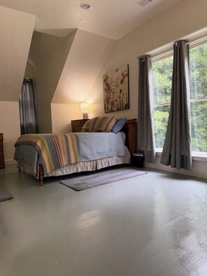 A bedroom with a bed, a nightstand, a lamp, a window with curtains, and a painting on the wall. - Over the Creek and Thru the Woods. Comfy 2BR/2bath. Sleeps9 .Firepit/pond (Abbeville)