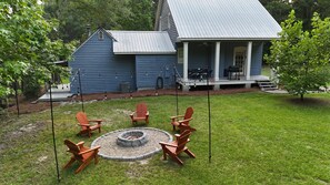 A blue house with a porch, a fire pit, and four Adirondack chairs.