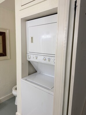A compact laundry room with a built-in washer and dryer, a toilet, and a framed picture on the wall.