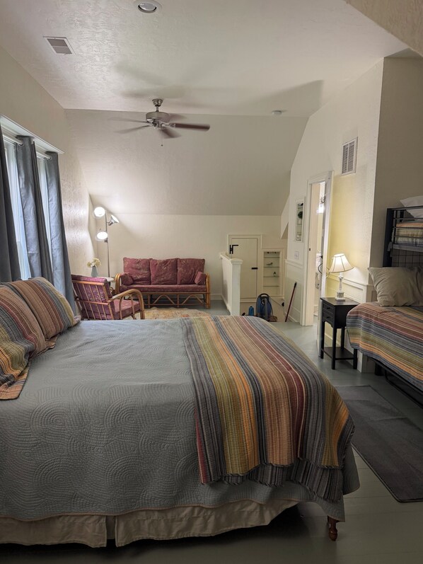 A bedroom with a large bed, a chair, a desk, and a ceiling fan.