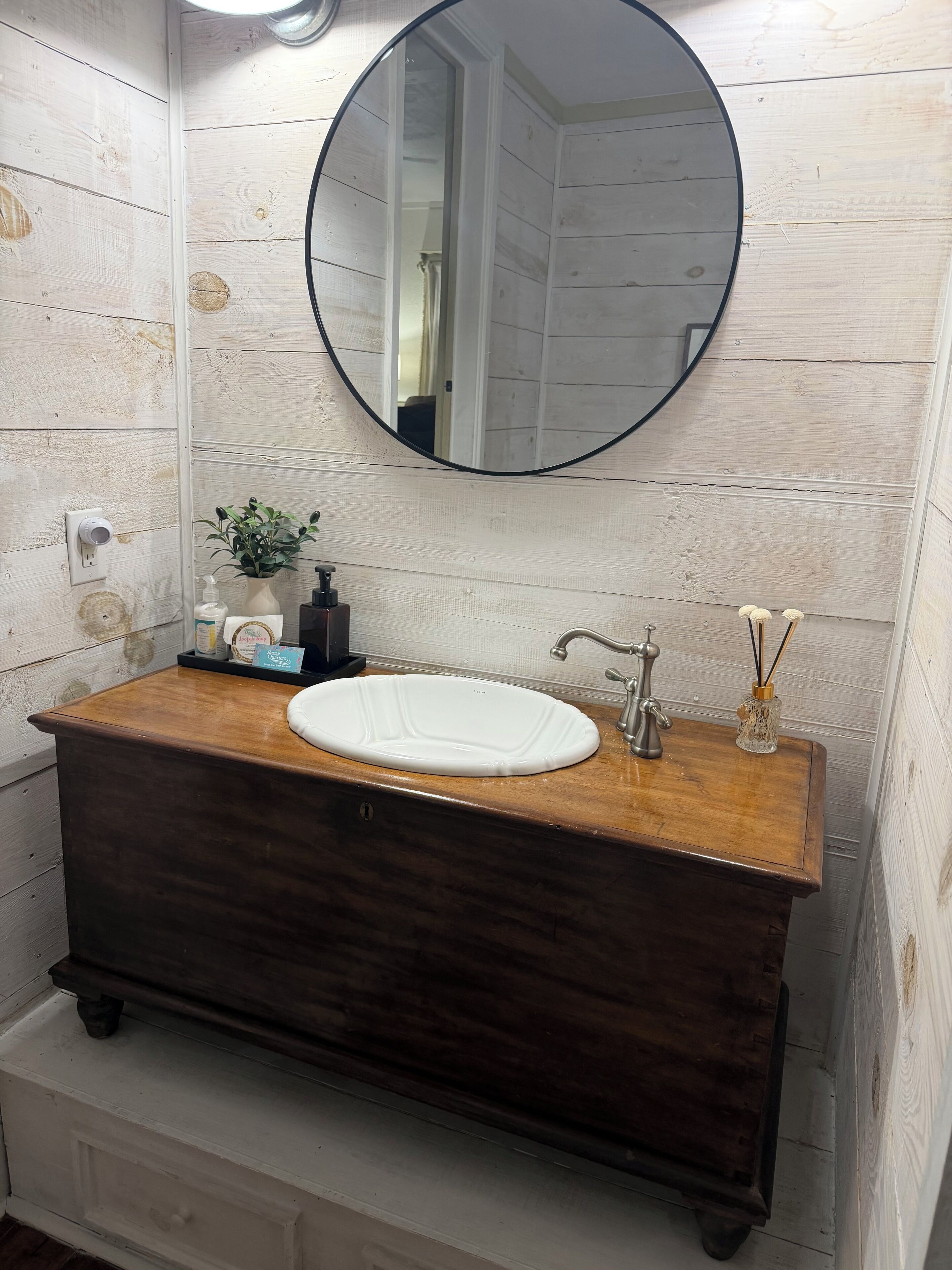 Een badkamer met een houten wastafel, een witte wasbak en een ronde spiegel.