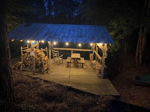 A wooden deck with a covered picnic area, benches, and a stack of firewood. - Over the Creek and Thru the Woods. Comfy 2BR/2bath. Sleeps9 .Firepit/pond (Abbeville)