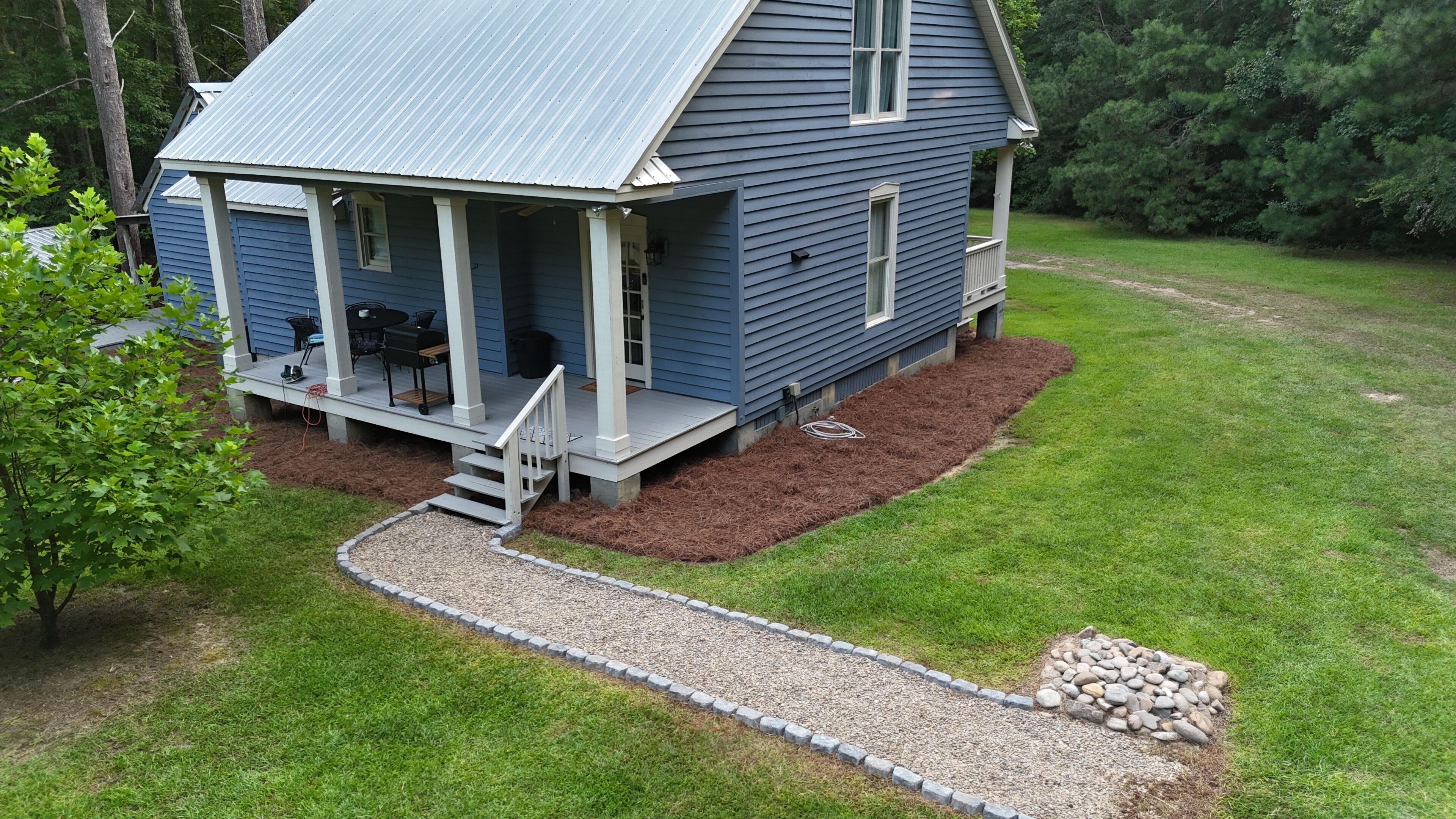 A two-story house with a porch, a small deck, and a gravel pathway leading to the entrance.