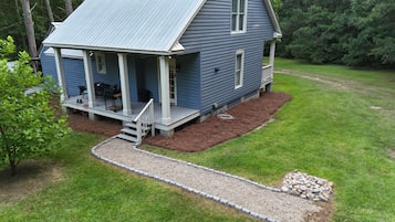 A two-story house with a porch, a small deck, and a gravel pathway leading to the entrance.