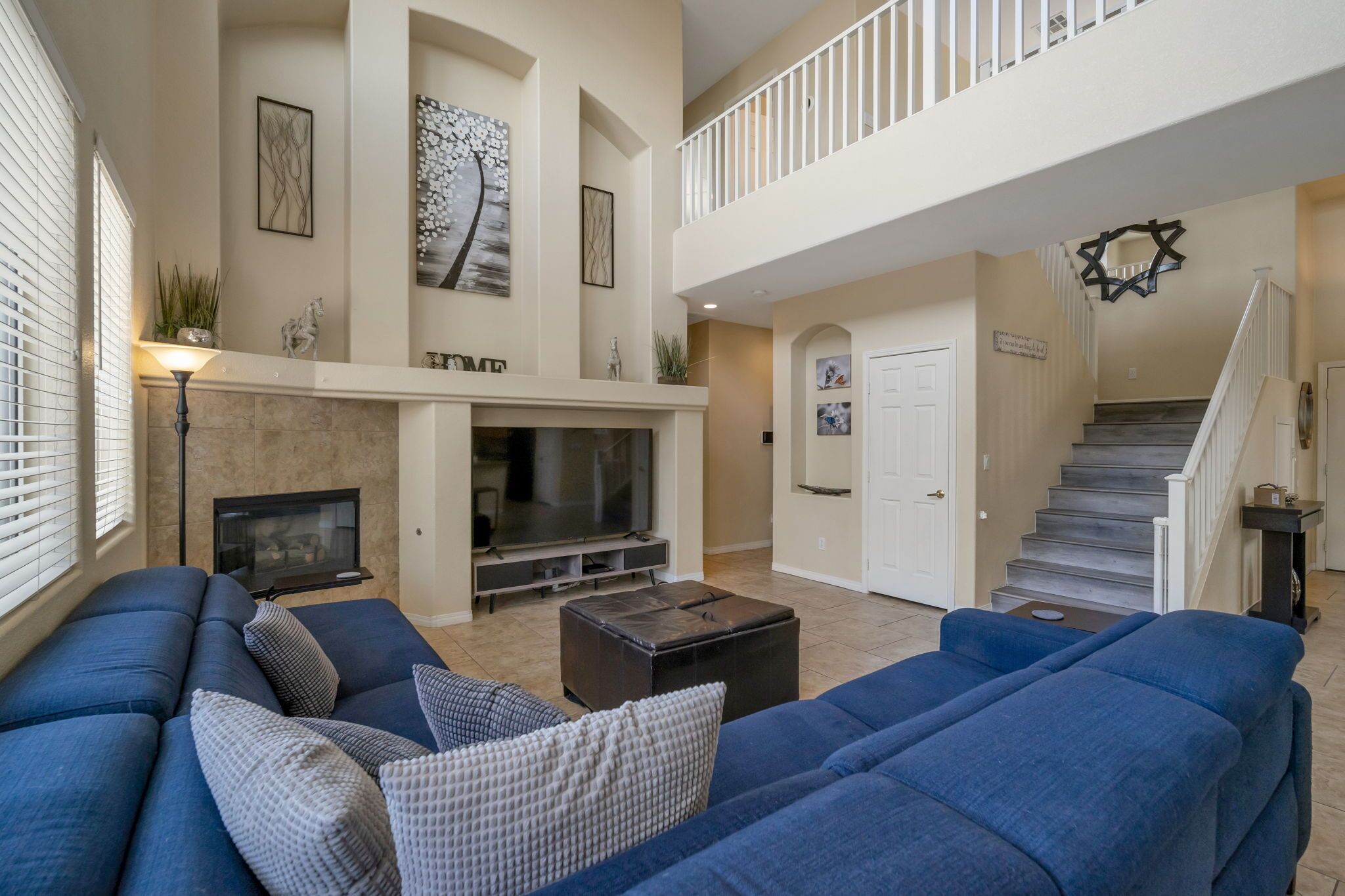 A spacious living room with a fireplace, a staircase, and a balcony.