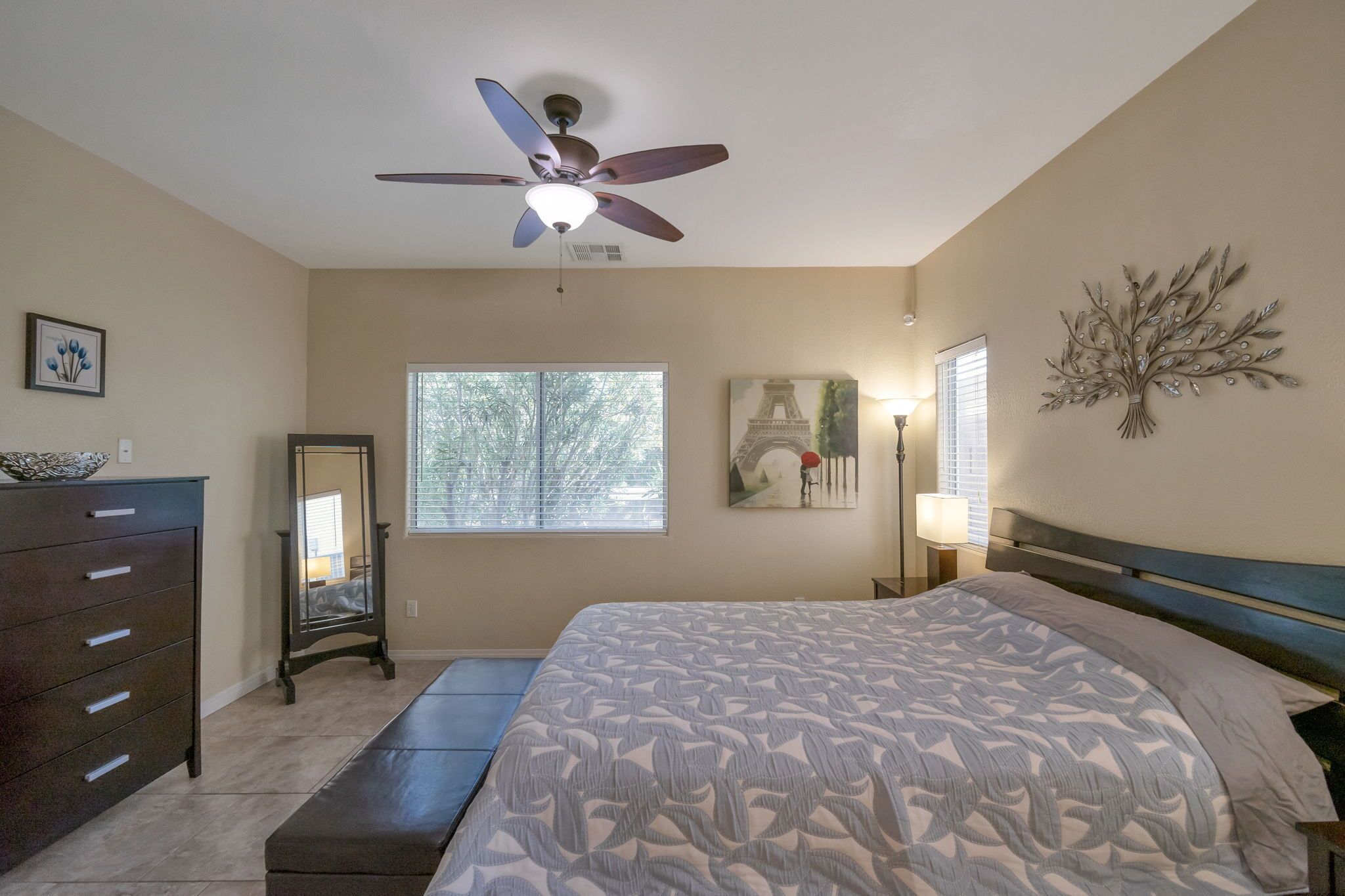 A bedroom with a bed, a dresser, a ceiling fan, a window, and wall art.