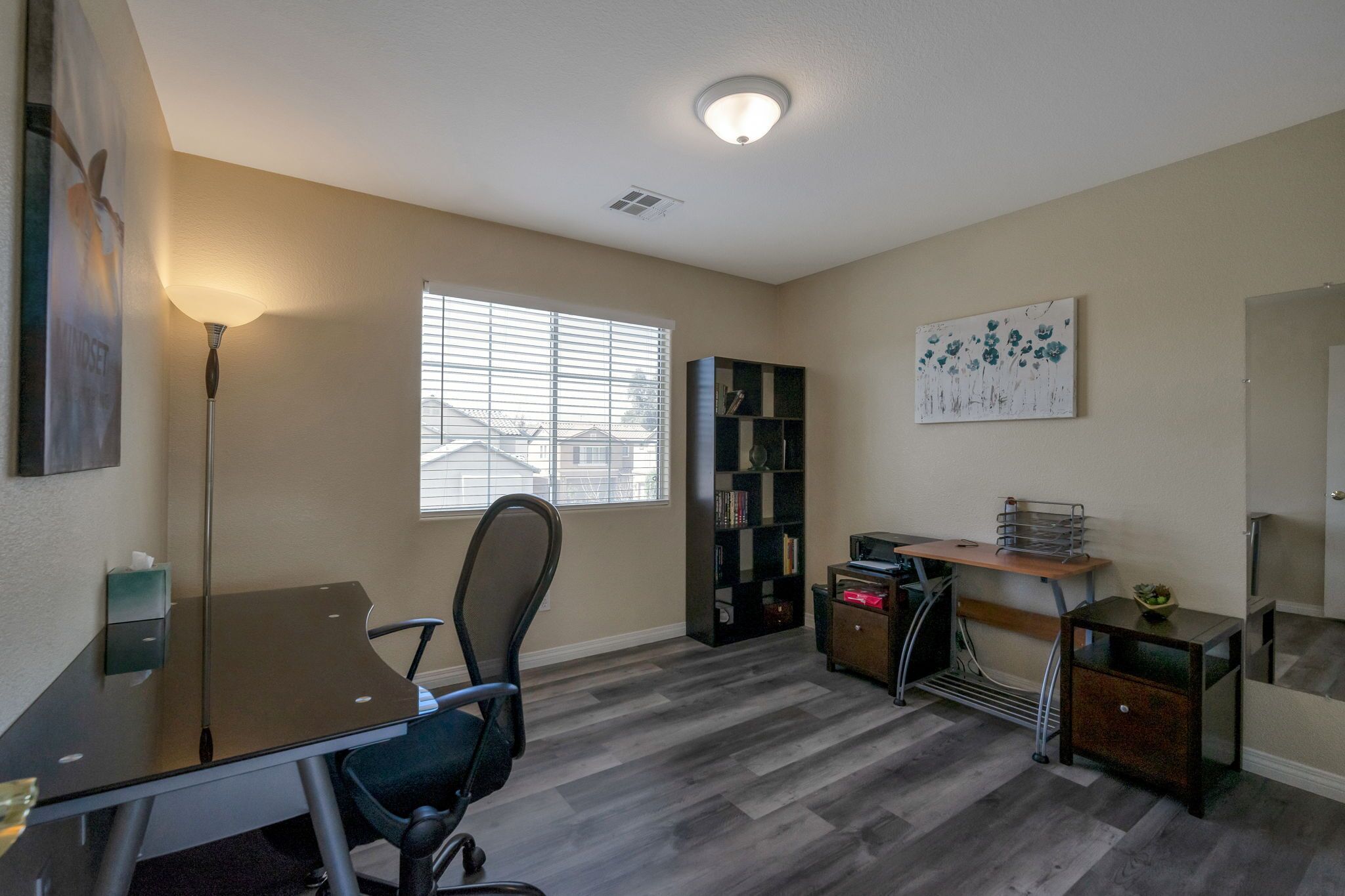A home office with a desk, chair, bookshelf, and a window with blinds.