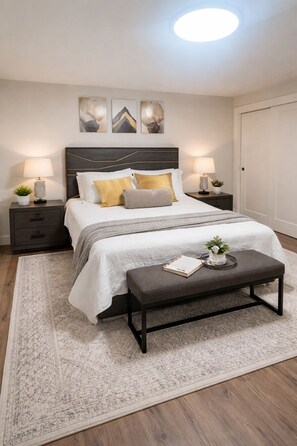 Une chambre à coucher avec un lit, des tables de chevet, un banc, un tapis et des œuvres d’art accrochées au mur.
