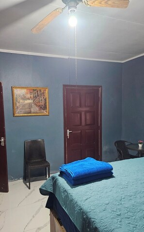 Ein Schlafzimmer mit Bett, einer Tür, einem Sessel, einem Deckenventilator und einem Bild an der Wand.