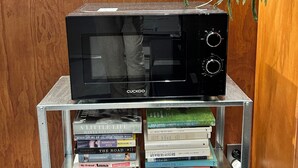 A microwave on a metal shelf with a collection of books underneath.