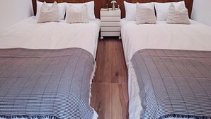 A hotel room with two beds, a wooden headboard, a nightstand with a lamp, and a plant.